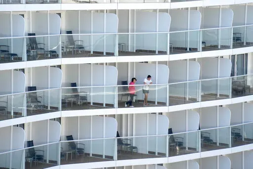 Passengers look out from the Spectrum of the Seas cruise ship docked at Kai Tak cruise terminal in Hong Kong Wednesday, Jan. 5, 2022. Thousands of passengers were being held Wednesday on the cruise ship in Hong Kong for coronavirus testing after health authorities said nine passengers were linked to a recent omicron cluster and ordered the ship to turn back. (AP Photo/Vincent Yu)