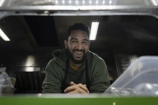 World Central Kitchen Chef Corp member Daniel Shemtob smiles as he looks out from the service window of his food truck, The Lime Truck, as he serves burritos to Eaton Fire first responders at the Rose Bowl Stadium, Wednesday, Jan. 15, 2025, in Pasadena, Calif. (AP Photo/Carolyn Kaster)
