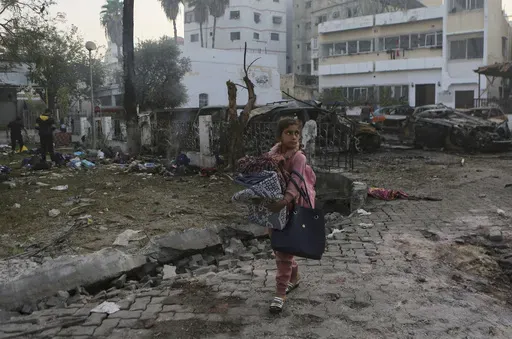 A Palestinian girl carries a blankets as she walks past the site of a deadly explosion at al-Ahli hospital, in Gaza City, Wednesday, Oct. 18, 2023. (AP Photo/Abed Khaled)
