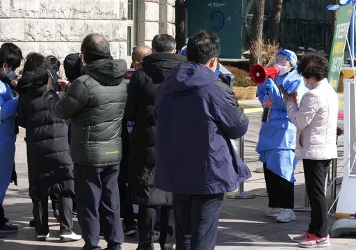 A medical worker uses a loud speaker to give advice to people as they wait for their coronavirus test at a makeshift testing site in Seoul, South Korea, Wednesday, Feb. 23, 2022. South Korean health officials on Wednesday approved Pfizer’s coronavirus vaccine for the country’s unvaccinated younger children, expanding its immunization program in the face of a massive omicron outbreak that is beginning to drive up hospitalizations and deaths. (AP Photo/Ahn Young-joon)