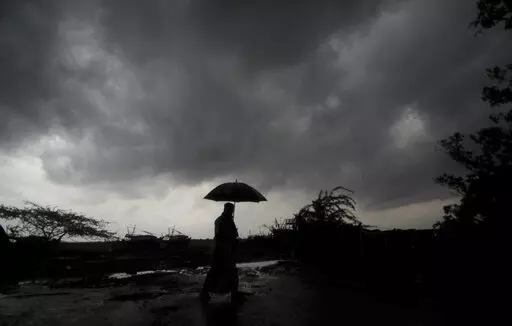 A villager holds an umbrella as dark clouds loom over Balasore district in Odisha, India, Tuesday, May 25, 2021, ahead of a powerful storm barreling toward the eastern coast. When it comes to measuring global warming, it’s not just the heat, it’s the humidity that matters in dangerous climate extremes, according to a study released on Monday, Jan. 31, 2022, in the Proceedings of the National Academy of Sciences in the U.S. (AP Photo/File)