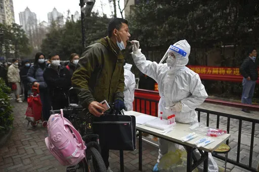 A man holding his bicycle with a school bag on it gets a throat swab during a mass COVID-19 test at a residential compound in Wuhan in central China's Hubei province, Tuesday, Feb. 22, 2022. Wuhan, the first major outbreak of the coronavirus pandemic has reported more than dozen new coronavirus cases this week, prompting the authority to step up precautious measures. (Chinatopix via AP)