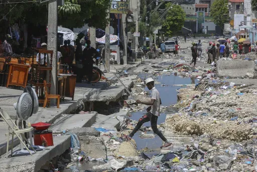 A man crosses a storm drain filled with trash in Port-au-Prince, Haiti, Friday, Sept. 13, 2024. (AP Photo/Odelyn Joseph)