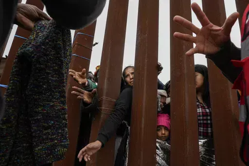 Migrants reach through a border wall for clothing handed out by volunteers as they wait between two border walls to apply for asylum Friday, May 12, 2023, in San Diego. Hundreds of migrants remain waiting between the two walls, many for days. The image was part of a series by Associated Press photographers Ivan Valencia, Eduardo Verdugo, Felix Marquez, Marco Ugarte Fernando Llano, Eric Gay, Gregory Bull and Christian Chavez that won the 2024 Pulitzer Prize for feature photography. (AP Photo/Greg