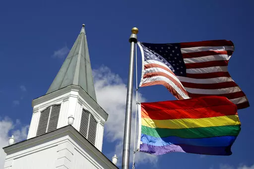 A gay pride rainbow flag flies along with the U.S. flag in front of the Asbury United Methodist Church in Prairie Village, Kan, on April 19, 2019.  A group of theologically conservative United Methodists plans to launch a new worldwide denomination on May 1, 2022.  This will begin the breakup of the third-largest religious body in the U.S.  (AP Photo/Charlie Riedel, File)