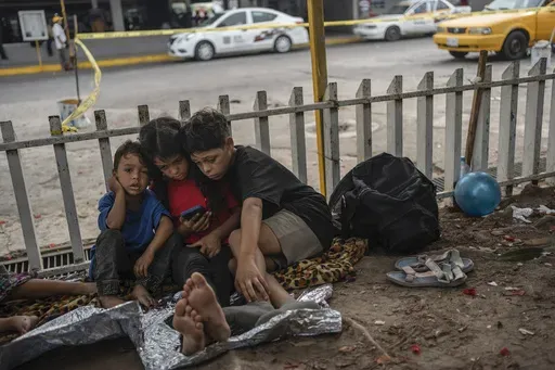 The Bolaños children, from left, Sebastian, Kamila and Miguel Angel, from Venezuela, watch videos on a mobile phone outside the bus terminal where they are living with their single mother Keilly and one other sibling, along with other migrants in Villahermosa, Mexico, June 8, 2024. Their mother was captured in the northern state of Juarez, where she said she was beaten by the military in front of her children, loaded on a bus for two days, and left in Villahermosa. (AP Photo/Felix Marquez, File