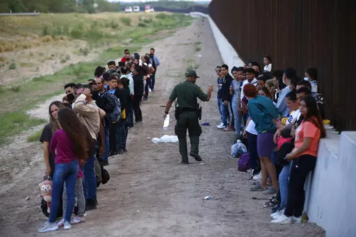A group of migrants stand next to the border wall as a Border Patrol agent takes a head count in Eagle Pass, Texas, Saturday, May 21, 2022. The Eagle Pass area has become increasingly a popular crossing corridor for migrants, especially those from outside Mexico and Central America, under Title 42 authority, which expels migrants without a chance to seek asylum on grounds of preventing the spread of COVID-19. (AP Photo/Dario Lopez-Mills, File)