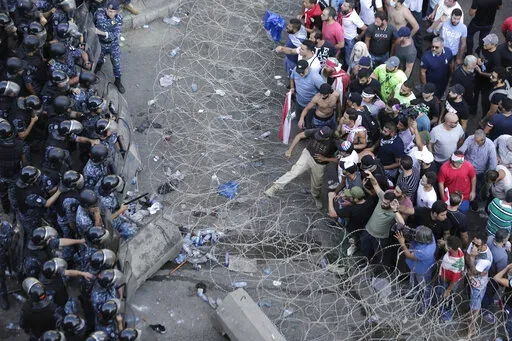 FILE- Riot police stand guard as anti-government protesters try to remove a barbed-wire barrier to advance towards the government buildings during a protest against a slate of new proposed taxes, including a $6 monthly fee for using Whatsapp voice calls, in Beirut, Lebanon, Saturday, Oct. 19, 2019. The measures set a spark to long smoldering anger against the ruling class and months of mass protests. Irregular capital controls were put in place, cutting people off from their savings as the curre