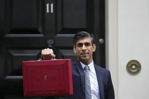 Britain's Chancellor of the Exchequer Rishi Sunak holds up the traditional ministerial red dispatch box as he leaves for the House of Commons to deliver the Budget in London, Oct. 27, 2021. Revelations that Prime Minister Boris Johnson and his staff partied while Britain was in a coronavirus lockdown have provoked public outrage and led some members of his Conservative Party to consider ousting their leader. If they manage to push Johnson out — or if he resigns — the party would hold a leade