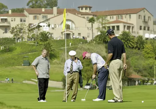 With the historic clubhouse in the background, Duffy Waldorf takes a practice putt at the 10th green as veteran teaching pro Eddie Merrins, in the tie, and golfer Arron Oberholser, right, watch during a practice session for the Nissan Open at Riviera Country Club, Feb. 18, 2003, in Los Angeles. Merrins died Wednesday, Nov. 22, 2023, at age 91. (AP Photo/Reed Saxon, File)