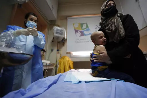 A woman holds her crying child at the cancer ward of the Children's Hospital in Damascus, Syria, Monday, March. 7, 2022. More than a decade of war has brought the Syrian health sector close to collapse, and an economic crisis has meant that cancer treatment is either unaffordable or in short supply. A private charity, Basma, offers cancer treatment without charge to impoverished Syrian children. (AP Photo/Omar Sanadiki)