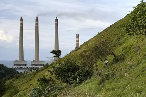 A couple walk on a hill called 'Teletubbies Hill', a locally popular tourist attraction, as the chimneys of Suralaya coal power plant looms in the background, in Cilegon, Indonesia, Sunday, Jan. 8, 2023. Asia must rapidly cut fossil fuel subsidies and plow more money into a clean energy transition to avoid catastrophic climate change that puts its own development at risk, according to a new report Thursday, April 27, from the Asian Development Bank. (AP Photo/Dita Alangkara)