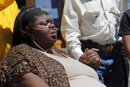 Kimberly Mcglothen, widow of Tommie McGlothen, Jr., holds the hand of his father, Tommie McGlothen, Sr., during a news conference with an attorney outside the Caddo Parish Courthouse in Shreveport, La., on  June 10, 2020. The trial of four officers charged in connection with the death of McGlothen, a man who died in police custody in northern Louisiana, will go forward, a judge ruled Thursday, Feb. 3, 2022, rejecting efforts by the four Shreveport officers to have the charges thrown out. (AP Pho