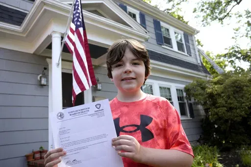 Danny Doherty, 12, of Norwood, Mass., stands for a photograph Wednesday, Aug. 21, 2024, in front of his home in Norwood, while holding a letter from the Town of Norwood Board of Health advising his family that they may not sell homemade ice cream at an ice cream stand near their home. (AP Photo/Steven Senne)