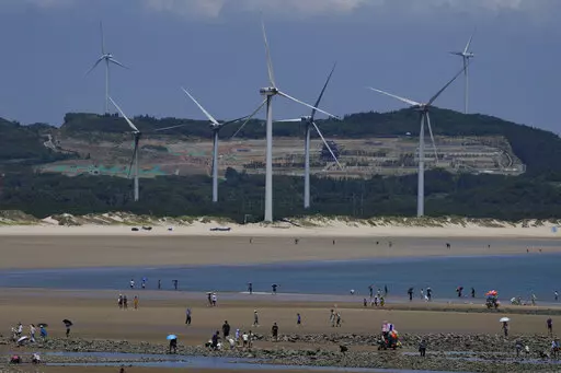 Beachgoers walk near wind turbines along the coast of Pingtan in Southern China's Fujian province, on Aug. 6, 2022. The world's two biggest emitters of greenhouse gases are sparring on Twitter over climate policy, with China asking if the U.S. can deliver on the landmark climate legislation signed into law by President Joe Biden this week. (AP Photo/Ng Han Guan)