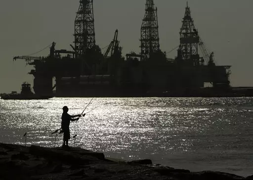 A man wears a face mark as he fishes near docked oil drilling platforms, on May 8, 2020, in Port Aransas, Texas. A federal court has rejected a proposed lease auction for offshore oil drilling in the Gulf of Mexico, saying the Biden administration failed to conduct a proper environmental review. The decision on Jan. 27, 2022, by U.S. District Judge Rudolph Contreras sends the proposed lease sale back to the Interior Department to decide next steps. (AP Photo/Eric Gay, File)