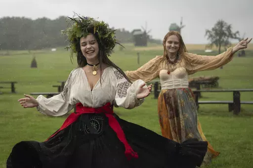 Ukrainian young women dressed in traditional clothing dance under heavy rain at a traditional Midsummer Night celebration near capital Kyiv, Ukraine, Sunday, June 23, 2024. The age-old pagan festival is still celebrated in Ukraine amid the third year of Russia-Ukraine war. (AP Photo/Efrem Lukatsky)