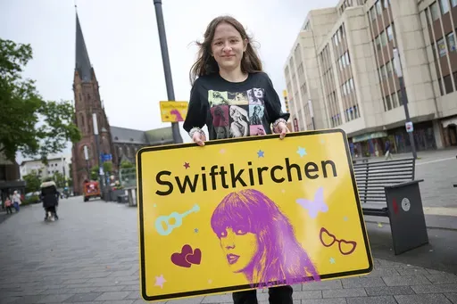 Schoolgirl Aleshanee Westhoff shows a "Swiftkirchen" town sign in honor of musician Taylor Swift in Gelsenkirchen, Germany, Tuesday, July 2, 2024. The Swifties are about to take over the German city of Gelsenkirchen, where American superstar Taylor Swift is set to give three concerts of her Eras Tour later this month. In honor of the singer, the city renamed itself “Swiftkirchen" — at least temporarily to welcome the tens of thousands of fans who are expected to come for the Eras Tour shows 