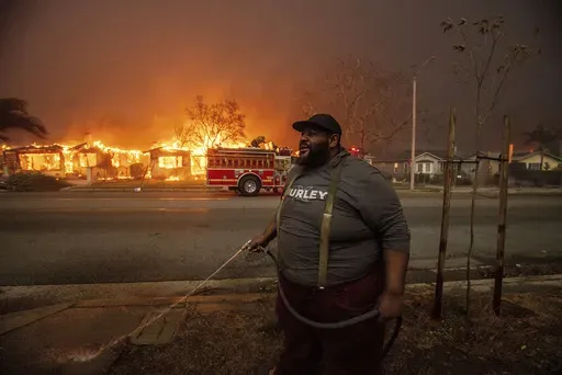 A resident sprays their property with a garden hose as the Eaton Fire engulfs structures across the street, Wednesday, Jan. 8, 2025 in Altadena, Calif. (AP Photo/Ethan Swope, File)