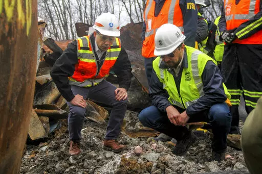 Transportation Secretary Pete Buttigieg, left, and Tristan Brown, deputy administrator of the Pipeline and Hazardous Materials Safety Administration, crouch down to look at part of a burned traincar, Thursday, Feb. 23, 2023, in East Palestine, Ohio, at the site of a Norfolk Southern train derailment. (Allie Vugrincic/The Vindicator via AP, Pool)