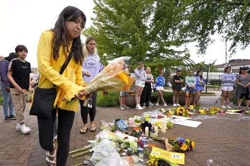 Yesenia Hernandez, granddaughter to Nicolas Toledo, who was killed during Monday's Highland Park., Ill., Fourth of July parade, brings flowers to a memorial for Toledo and six others who lost their lives in the mass shooting, Wednesday, July 6, 2022, in Highland Park. (AP Photo/Charles Rex Arbogast)