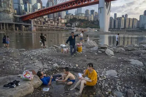 People sit in a shallow pool of water in the riverbed of the Jialing River, a tributary of the Yangtze, in southwestern China's Chongqing Municipality, Saturday, Aug. 20, 2022. The very landscape of Chongqing, a megacity that also takes in surrounding farmland and steep and picturesque mountains, has been transformed by an unusually long and intense heat wave and an accompanying drought. (AP Photo/Mark Schiefelbein)