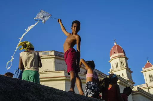 A youth flies a kite outside the shrine of the Virgin of Charity of Cobre in El Cobre, Cuba, on Saturday, Feb. 10, 2024. The Vatican-recognized Virgin, venerated by Catholics and followers of Afro-Cuban Santeria traditions, is at the heart of Cuban identity, uniting compatriots from the Communist-run Caribbean island to those who were exiled or emigrated to the U.S. (AP Photo/Ramon Espinosa)