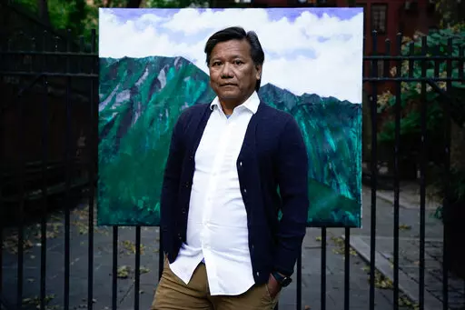 Bobby Calvan poses in front of a painting of the view from his childhood home in Waimanalo, Hawaii, Sunday, Oct. 9, 2022, in New York. His journey out of the closet has taken decades. Now 57, he is still sharing his truth about his sexuality. The journey hasn’t ended; indeed, it’s just beginning as he now lives his life as the man he believes he was meant to be. (AP Photo/Julia Nikhinson)