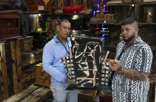 Artisans Adrian Moran, left, and Ariel Sanchez, the creators of Clave Humidors, pose with one o their cigar humidifiers during the XXV Cigar Festival at Convention Palace in Havana, Monday, Feb. 24, 2025. (AP Photo/Ramon Espinosa)