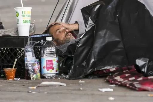 A man in a homeless encampment lays among possessions after Louisiana State police gave instructions for them to move to a different pre-designated location as they perform a sweep in advance of a Taylor Swift concert in New Orleans, Wednesday, Oct. 23, 2024. (AP Photo/Gerald Herbert)