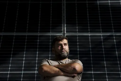 Sebastian Tirintica sits backdropped by solar panels in the RenewAcad training center in Petrosani, southern Romania, Friday, Oct. 11, 2024. (AP Photo/Vadim Ghirda)