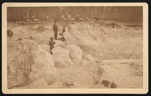 Photograph shows two white men overseeing African American men hammering boulders as others walk with wheelbarrows in a shallow pit phosphate mine, Dunnellon, Florida, 1890. (Library of Congress via AP)
