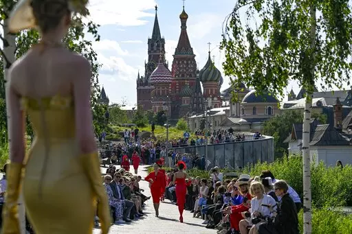 A model displays the collection by Russian designer Slava Zaitsev during the opening of the Fashion Week in at Zaryadye Park with the Spasskaya Tower and St. Basil's Cathedral in the background near Red Square in Moscow, Russia, Monday, June 20, 2022. Chic and adventurous models and couturiers have been spread all over the Russian capital for Moscow Fashion Week, flaunting their designs in venues ranging from a sprawling Stalin-era propaganda exposition to a large park near the Kremlin admired f