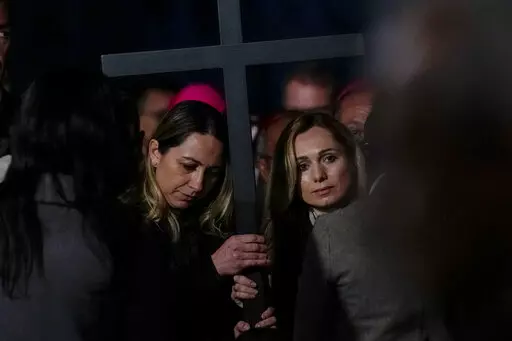Two nurses, Albina from Russia, right, and Irina, from Ukraine hold the cross as they take part in the Via Crucis (Way of the Cross) torchlight procession presided by Pope Francis on Good Friday in front of Rome's Colosseum, in Rome, Friday, April 15, 2022. (AP Photo/Gregorio Borgia)