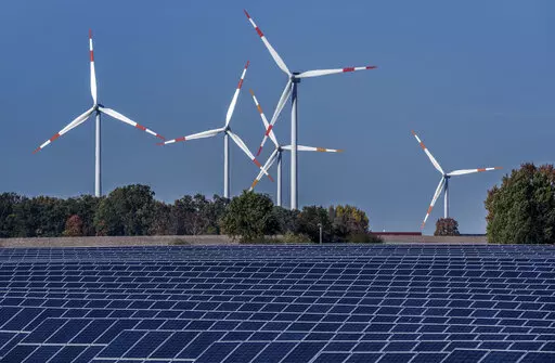 Wind turbines turn behind a solar farm in Rapshagen, Germany, Thursday, Oct. 28, 2021. Proponents of clean energy and thinks tanks have long said it's possible to reduce emissions and keep an economy growing. Now the latest report from the world's top climate scientists says 18 countries have done just that, sustaining emissions reductions “for at least a decade” as their economies continued to grow. (AP Photo/Michael Sohn, File)