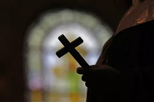 This Dec. 1, 2012 file photo shows a silhouette of a crucifix and a stained glass window inside a Catholic Church in New Orleans. On Thursday, Sept. 7, 2023, a Louisiana state grand jury charged a now-91-year-old disgraced priest, Lawrence Hecker, with sexually assaulting a teenage boy in 1975, an extraordinary prosecution that could shed new light on what Roman Catholic Church leaders knew about a child sex abuse crisis that persisted for decades and claimed hundreds of victims. (AP Photo/Geral