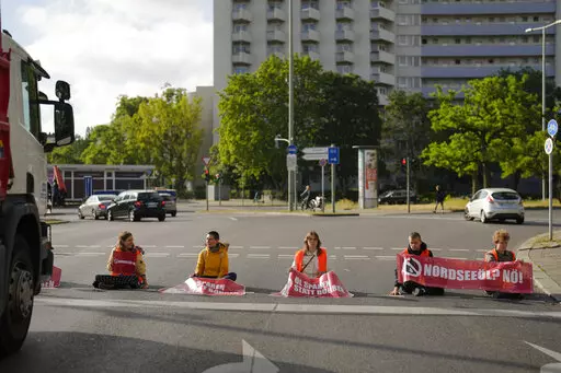 Climate activist Lina Schinkoethe, left, and her mother Solvig Schinkoethe, second from left, sit with their hands glued to the ground during a protest with the group Uprising of the Last Generation in Berlin, Germany, Tuesday, June 21, 2022. The group claims the world has only a few years left to turn the wheel around and avoid catastrophic levels of global warming.  (AP Photo/Markus Schreiber)