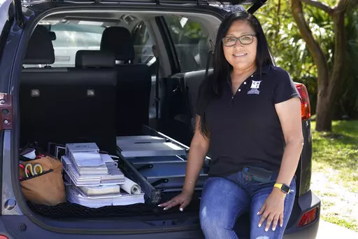 Natalia Ponce De Leon, owner of Custom Window Furnishings, sits on the back of her nine-year-old Toyota RAV4 after visiting with a client, Wednesday, April 13, 2022, in Delray Beach, Fla. Ponce De Leon traded her 2018 Toyota Tacoma for a more efficient car where she estimates will save her hundreds of dollars a month. She is also able to carry all the tools she needs for her business. (AP Photo/Marta Lavandier)