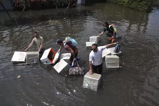 People try and save valuables as they wade through flood waters in the Edgewood neighborhood of Fort Lauderdale, Fla., April 13, 2023. Over 25 inches of rain fell in South Florida since Monday, causing widespread flooding. (Joe Cavaretta/South Florida Sun-Sentinel via AP)