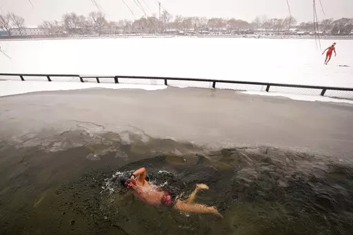 A man swims in the half-frozen water at the Shichahai Lake during a snow fall in Beijing, Sunday, Feb. 13, 2022. According to some of the local residents, swimming in the freezing water leads to health. (AP Photo/Andy Wong)