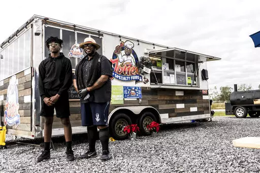 Mike Jones poses with his son Stephen MJ Jones Jr. in front of their food truck in Gray, La,, on Dec. 21, 2021. (Kezia Setyawan/The Courier via AP)