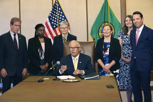 Gov. Jay Inslee signs Senate Bill 5536 concerning controlled substances on Tuesday, May 16, 2023, in Olympia, Wash. Behind him are from left to right: Rep. Roger Goodman, D- Kirkland, Rep. Jamila Taylor, D-Federal Way, House Speaker Laurie Jinkins, D-Tacoma, June Robinson, D-Everett, an identified woman and Andy Billig, D-Spokane. The policy, approved by Washinton lawmakers and signed by Inslee, keeps controlled substances illegal while boosting resources to help those struggling with addiction.