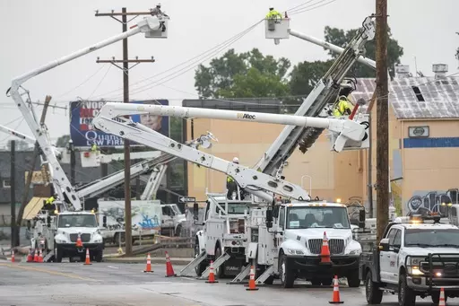 Line workers in boom trucks and on the street work to replace broken utility poles and lines as rain moves in on Peoria Avenue over the Broken Arrow Expressway, Wednesday, June 21, 2023, in Tulsa, Okla. (Daniel Shular/Tulsa World via AP)