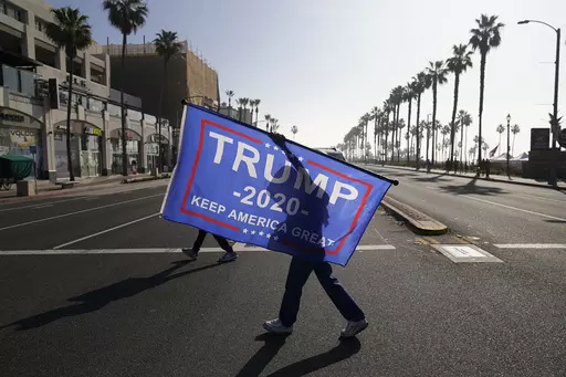 A woman walks across the street with a flag supporting President Donald Trump during a rally Jan. 6, 2021, in Huntington Beach, Calif. A state GOP rule change has opened the possibility that former President Donald Trump could sweep California’s entire trove of delegates in the March 5 primary, the plumpest prize in the party’s nominating contest. The election falls on Super Tuesday, when California is among more than a dozen states holding primaries and the largest number of delegates are u