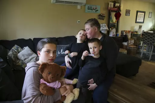 Jillian Philips sits with her children Macy, 10, and 4-year old twins, Emmett and Jude, right, in their home, Tuesday, May 2, 2023, in North Brookfield, Mass. Macy holds a teddy bear that houses a silver heart-shaped urn with some of the ashes of her deceased sister, Emilia, who died at 5 days old in 2015. Philips, who used the drug Mifepristone to manage her miscarriage, is concerned that other women who miscarry could suffer if the pill, also used for abortions, is taken off the market. (AP Ph