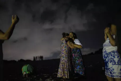 Mag Oliveira embraces her daughter Najla as they pray in an area of the Abaete dune system, on a steep rise of sand evangelicals have come to call the "Holy Mountain", in Salvador, Brazil, late Friday night, Sept. 16, 2022. Evangelicals have been converging on the dunes for some 25 years but especially lately, with thousands now coming each week to sing, pray and enter trancelike states to commune with God.(AP Photo/Rodrigo Abd)