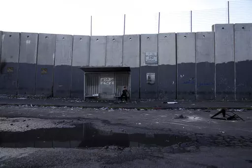 A child sits at a bus stop in the besieged Shuafat refugee camp in east Jerusalem, Thursday, Oct. 13, 2022.It was the site of fierce clashes after Israeli security forces set up checkpoints that choked off the only exit and entry points of the camp during a manhunt following the death of a soldier, bringing life to a standstill for its estimated 60,000 residents. (AP Photo/Mahmoud Illean)