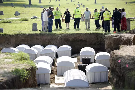 In this July 30, 2021 photo, a group prays during a small ceremony as remains from a mass grave are reinterred at Oaklawn Cemetery in Tulsa, Okla. People who believe they are descendants of Tulsa Race Massacre victims can now provide genetic material to help scientists try to identify remains of possible victims. The committee overseeing the search for mass graves of victims was told Tuesday, June 21, 2022, that enough usable DNA for testing has been found in two of the 14 sets of remains that w