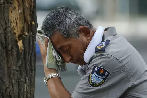 A security guard wearing an electric fan on his neck wipes his sweat on a hot day in Beijing, Monday, July 3, 2023. Heavy flooding has displaced thousands of people around China as the capital had a brief respite from sweltering heat. Beijing reported 9.8 straight days when the temperature exceeded 35 C (95 F), the National Climate Center said Monday. (AP Photo/Andy Wong)