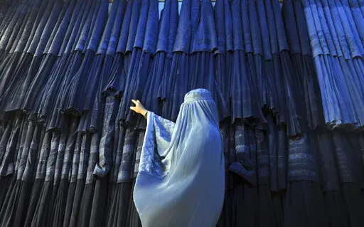 A woman clad in a burqa looks at other pieces of Afghanistan's traditional, all-encompassing dress at a store in Mazar-i Sharif, north of Kabul, Afghanistan, on Sept. 10, 2015. The Taliban announced they have arrested and will soon sentence an Afghan woman who appeared in a video on social media on Aug.  30, 2022, and said a senior Taliban official forced her into marriage and raped her repeatedly. (AP Photo/Mustafa Najafizada, File)